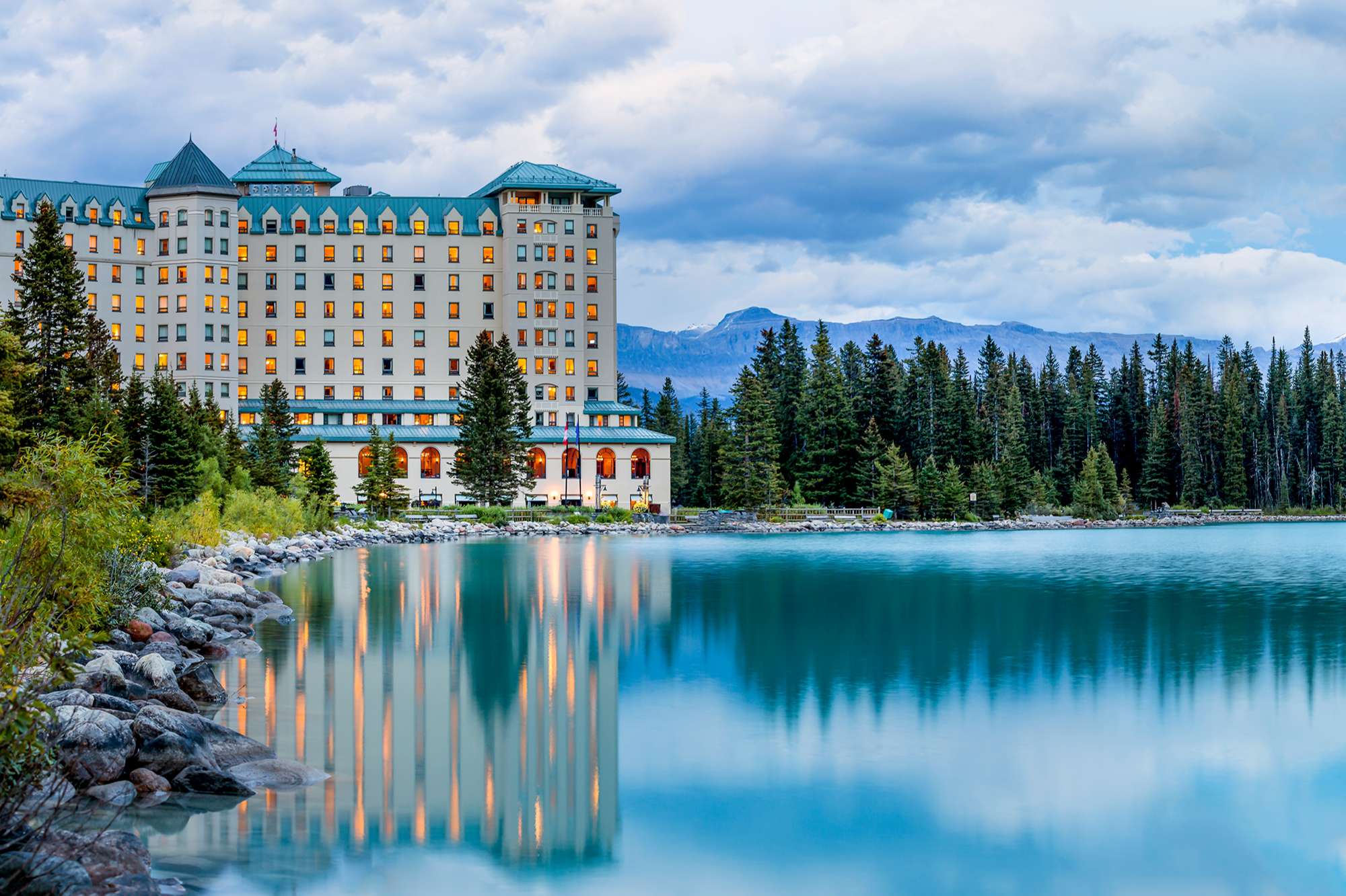 Fairmont Chateau Lake Louise, an iconic luxury mountain resort nestled in Alberta's Banff National Park. Surrounded by majestic mountain peaks, the glistening Victoria Glacier, and the serene emerald lake, it stands as a timeless retreat in the heart of nature.