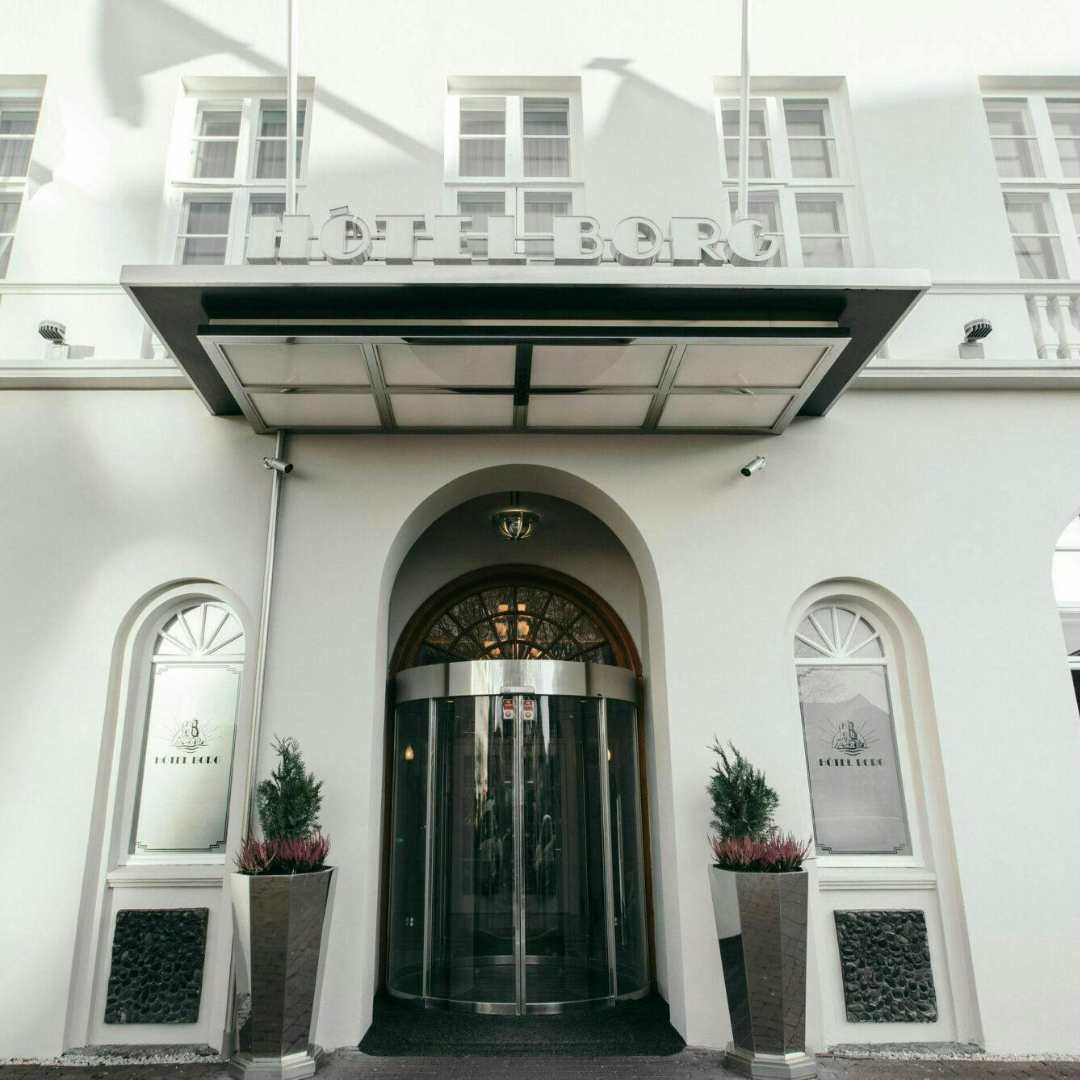 A captivating view of the luxurious entrance to Hotel Borg in Reykjavik, Iceland. The grandeur of the hotel is highlighted in the intricate details of the entrance, inviting guests into a world of elegance and sophistication. A blend of historic charm and modern luxury welcomes visitors to this iconic Icelandic destination.