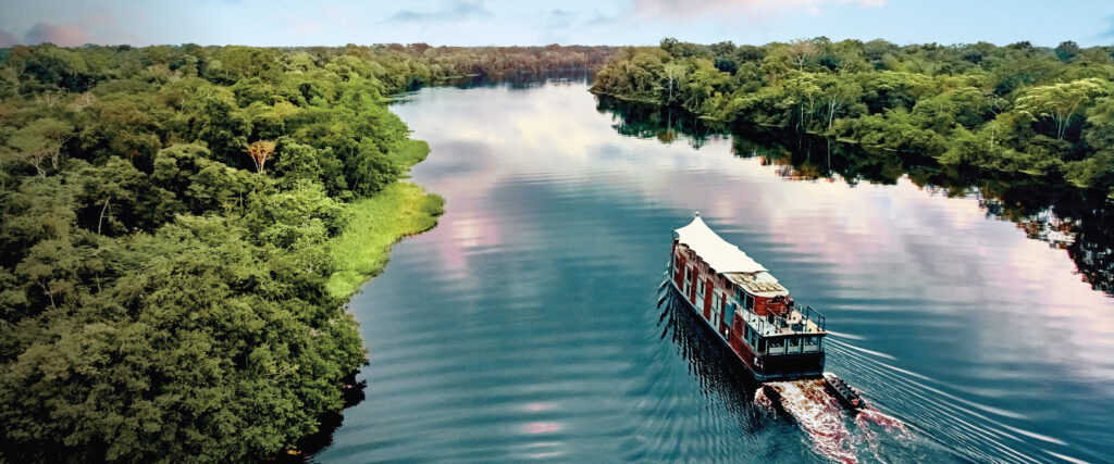 A captivating view of the M/V Amazon Aria gracefully cruising along the Amazon River in Peru, surrounded by lush rainforest and tranquil waters. A thrilling destination for self-flying pilots exploring South America