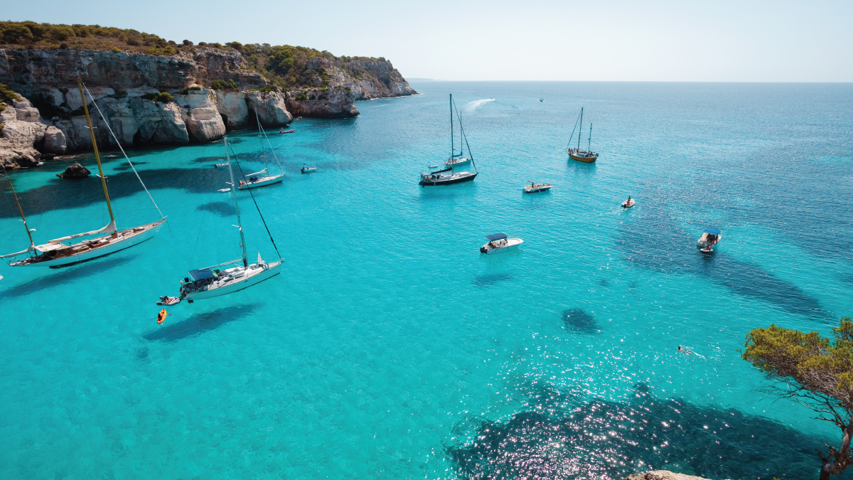 An enchanting aerial perspective of the coastal view of Menorca, Spain, featuring rugged cliffs, turquoise waters, and secluded beaches. Tailored for self-flying pilots planning a European adventure