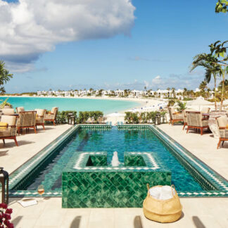 A tranquil scene of the pool at Belmond Cap Juluca in The Valley, Anguilla, surrounded by lush greenery and overlooking the azure Caribbean Sea. Tailored for self-flying pilots
