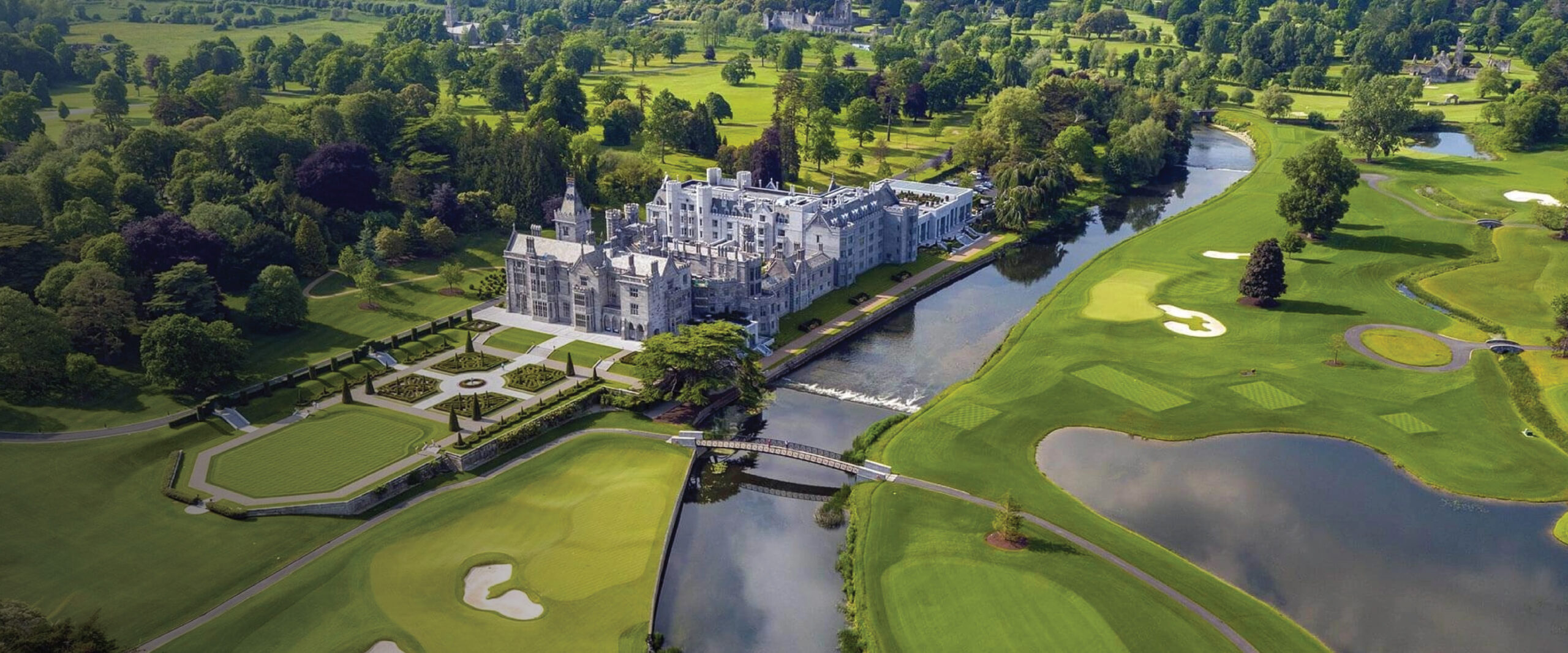 A mesmerizing aerial view of Adare Manor in Shannon, Ireland, nestled amidst lush greenery and rolling hills. Tailored for self-flying pilots planning a European adventure