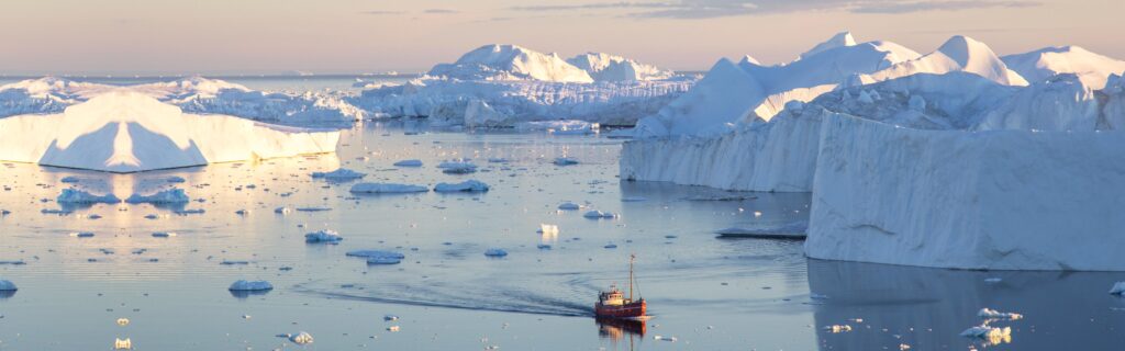 Little red sailboat cruising among floating icebergs in Disko Bay