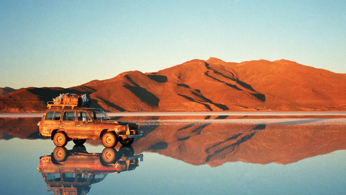 A captivating perspective of the Uyuni Salt Flats in Bolivia, with a truck traversing the vast expanse against the backdrop of the towering Andean Mountains. A remarkable destination for self-flying pilots exploring South America